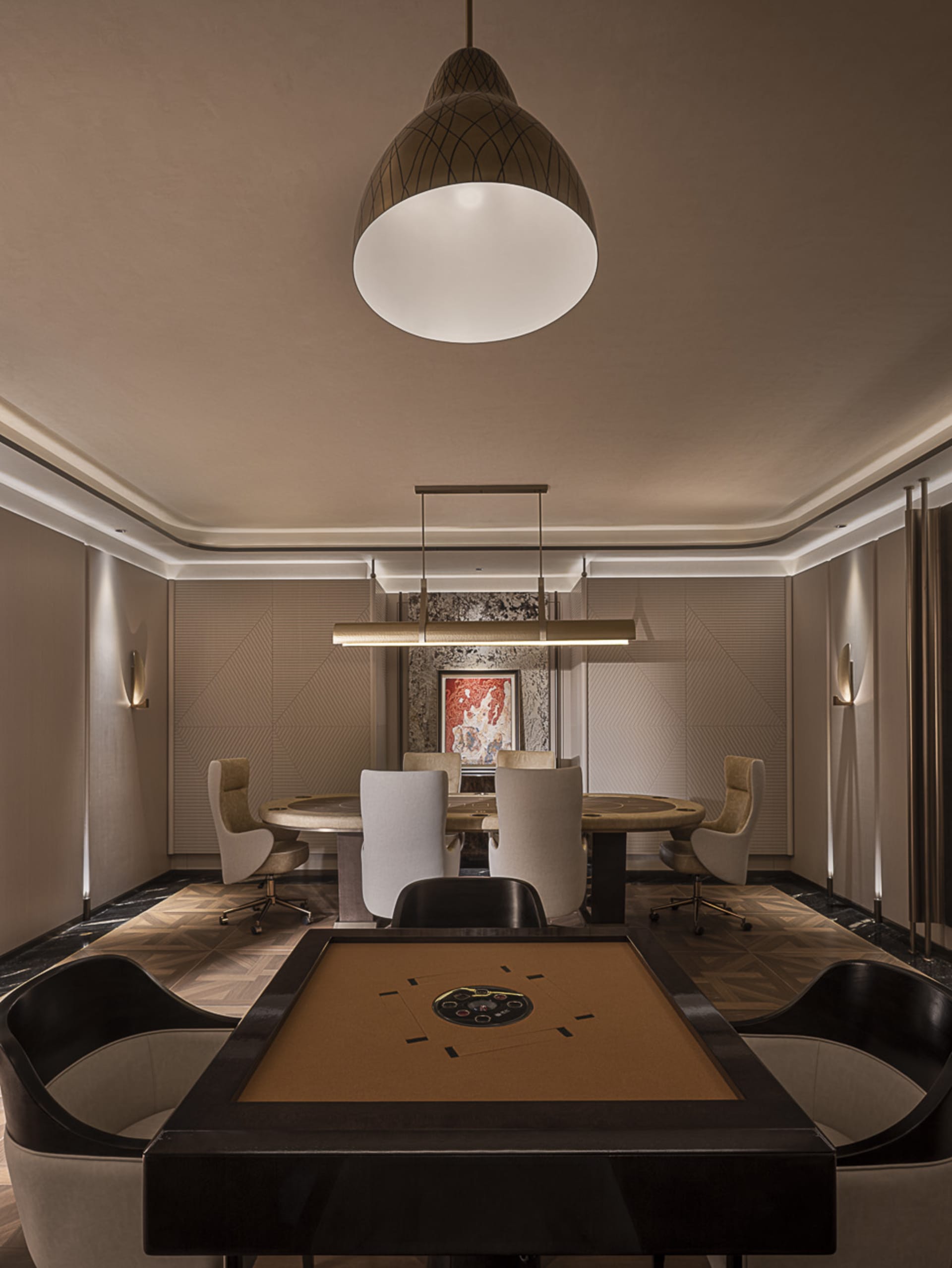 Elegant luxury mahjong parlor with a large square walnut table in the foreground, a round marble dining table with six upholstered swivel chairs in the background, geometric wall paneling, and a large pendant light.