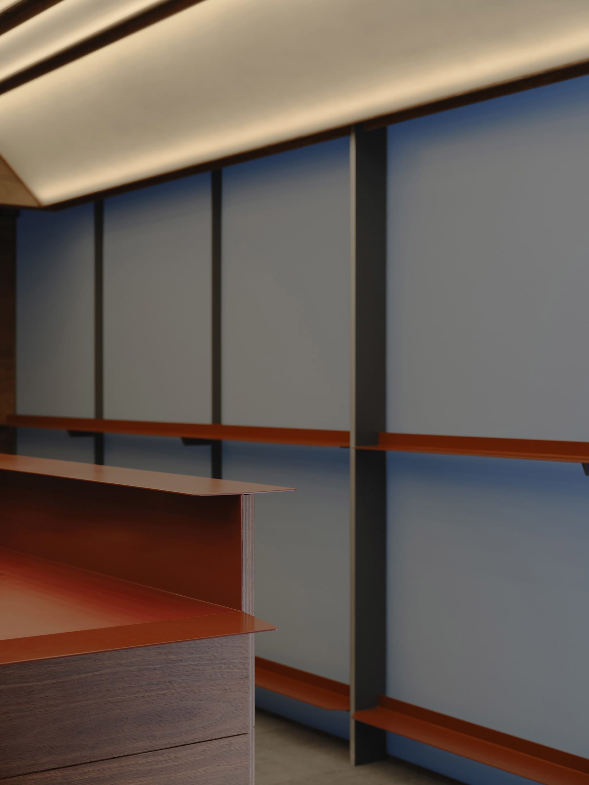 Close-up view of a modern walnut reception desk with integrated lighting and blue panel wall system with orange accents.