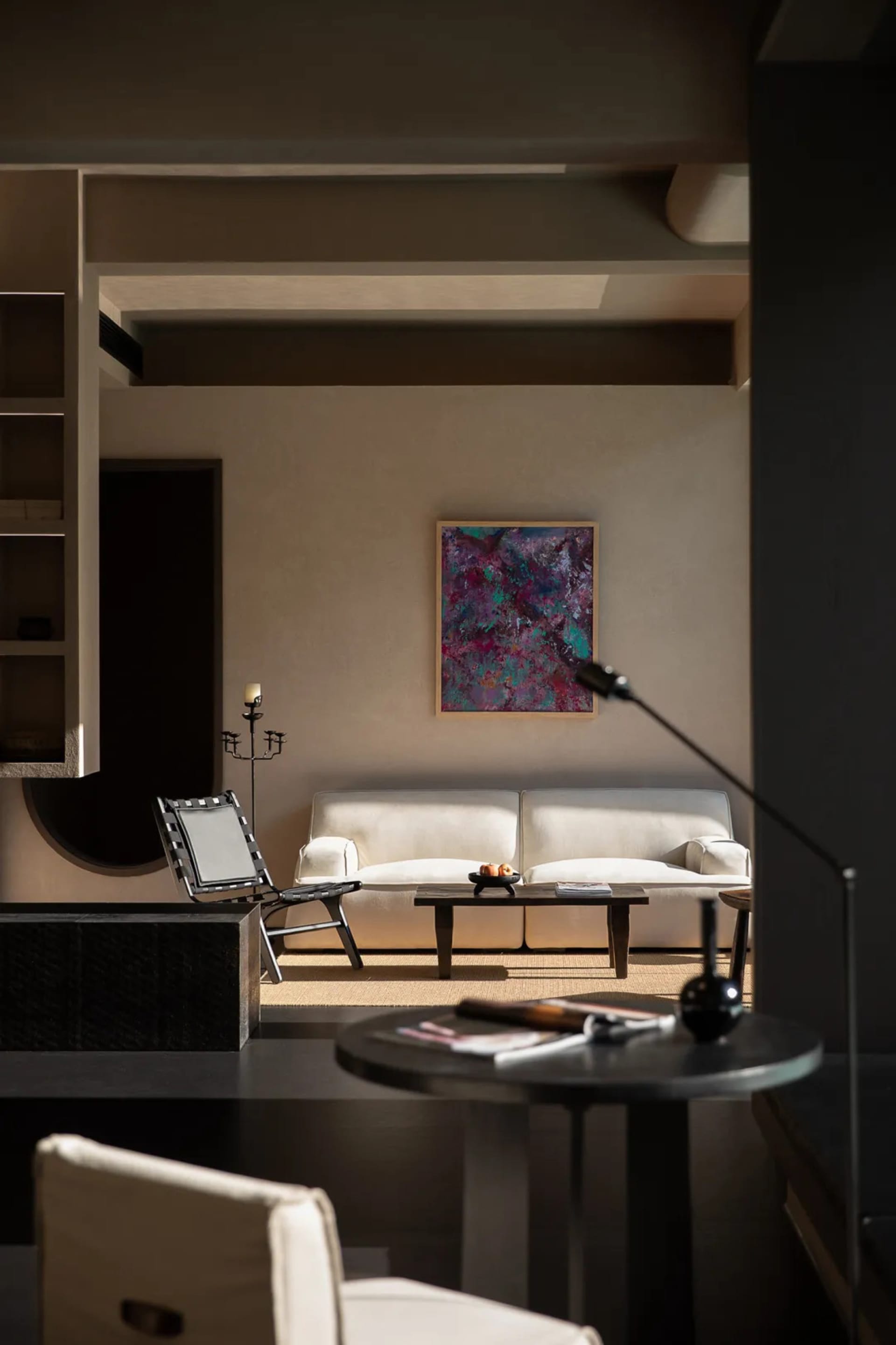 Modern minimalist living room featuring textured beige plaster walls, a white sofa, black woven chair, and a large colorful abstract painting.