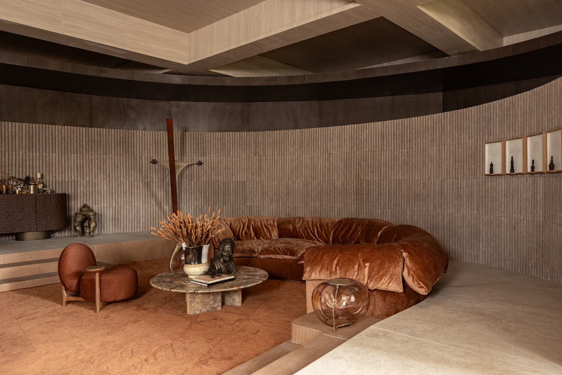 Modern living room featuring a large curved terracotta velvet sofa, marble coffee table, and curved wooden walls with warm earthy tones.
