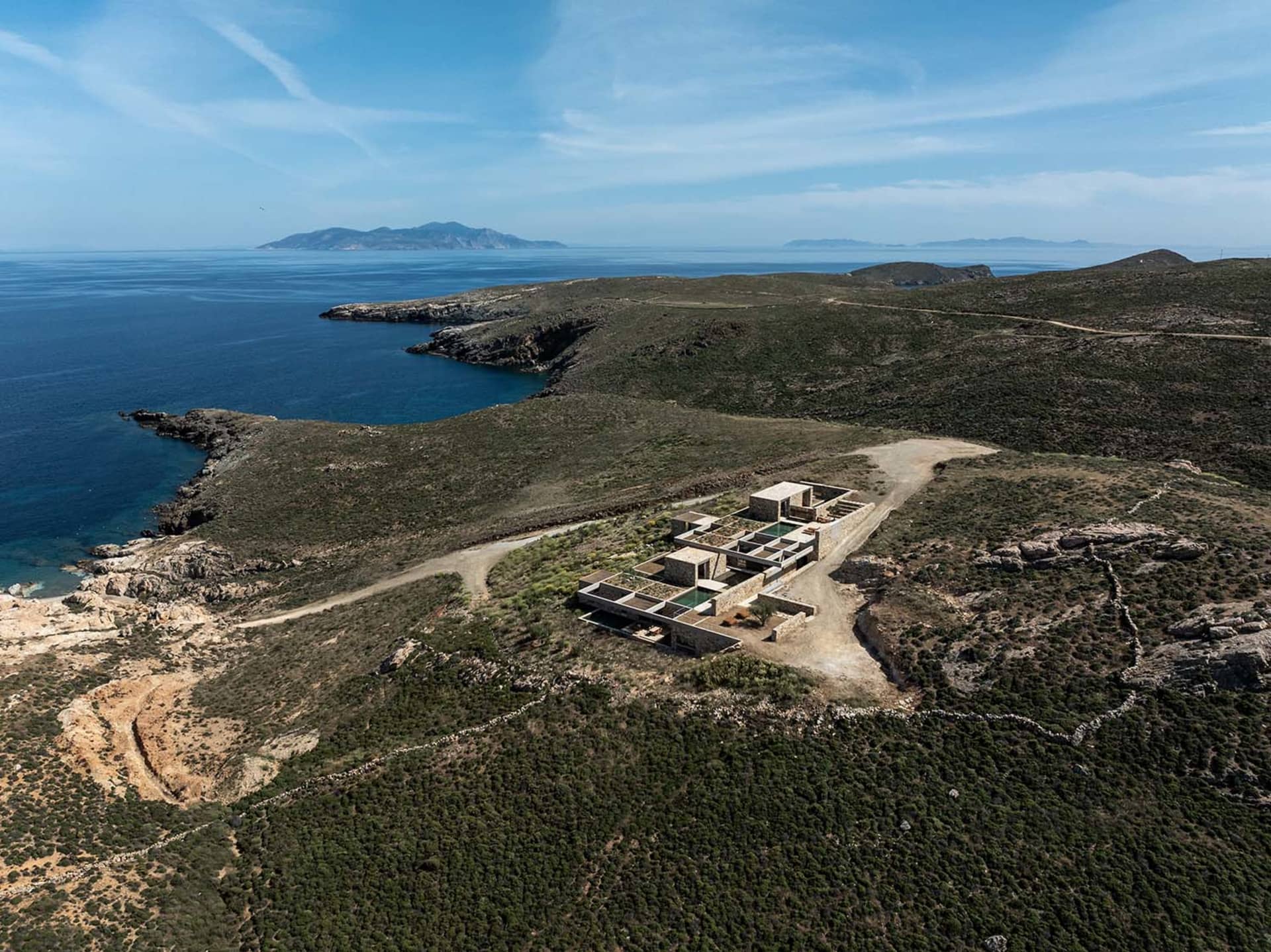Aerial view of a modern concrete villa built on a rocky cliff overlooking the deep blue Mediterranean sea under a clear sky.
