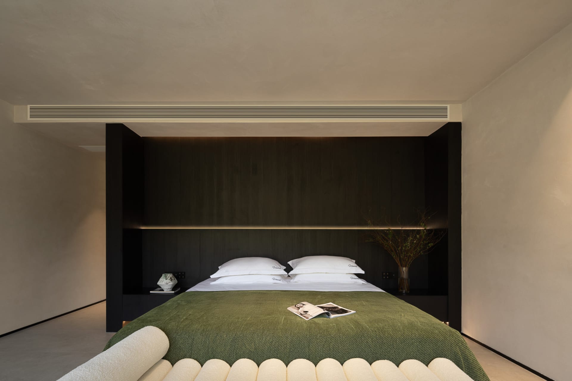 Modern minimalist bedroom with dark wood built-in headboard, white bedding, olive green textured throw blanket, and integrated LED lighting.