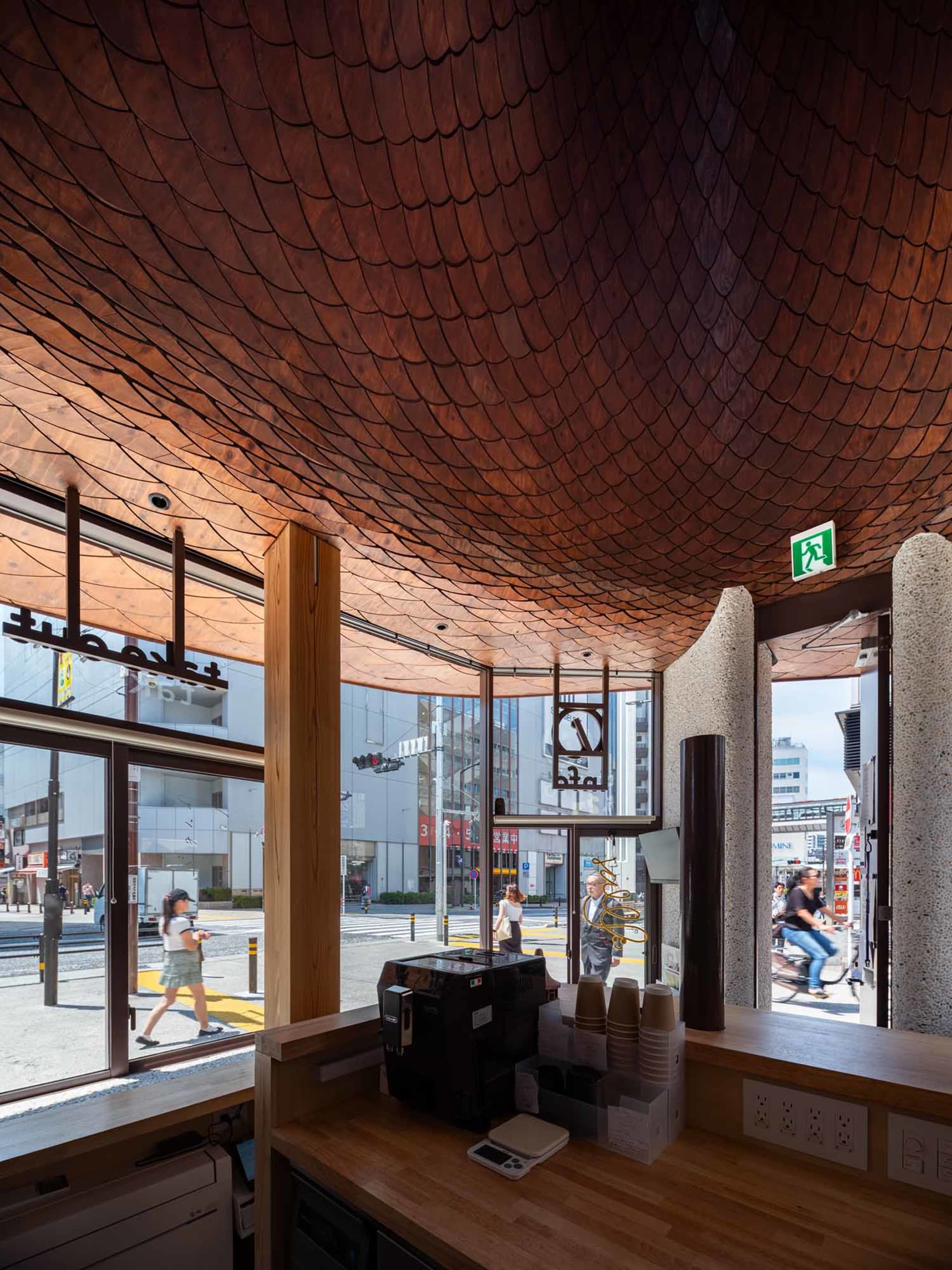 Interior view of a modern Tokyo cafe featuring a dramatic scalloped wooden ceiling, wooden service counter with coffee equipment, and large street-facing windows.
