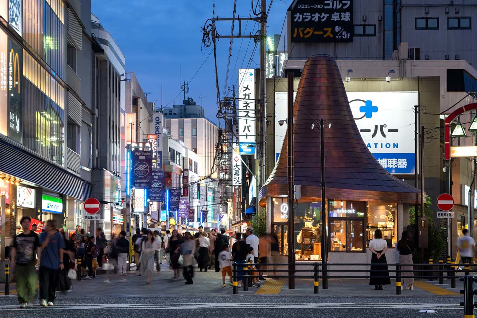 Busy pedestrian street in Shibuya at twilight featuring a distinctive cone-shaped copper kiosk, numerous neon signs, and crowds of people walking.