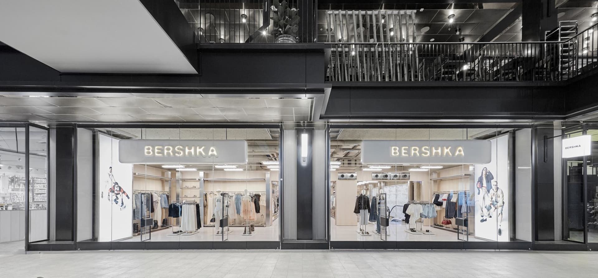 Modern Bershka retail store with full-height glass facade, black metal framing, and illuminated signage in a contemporary shopping mall.