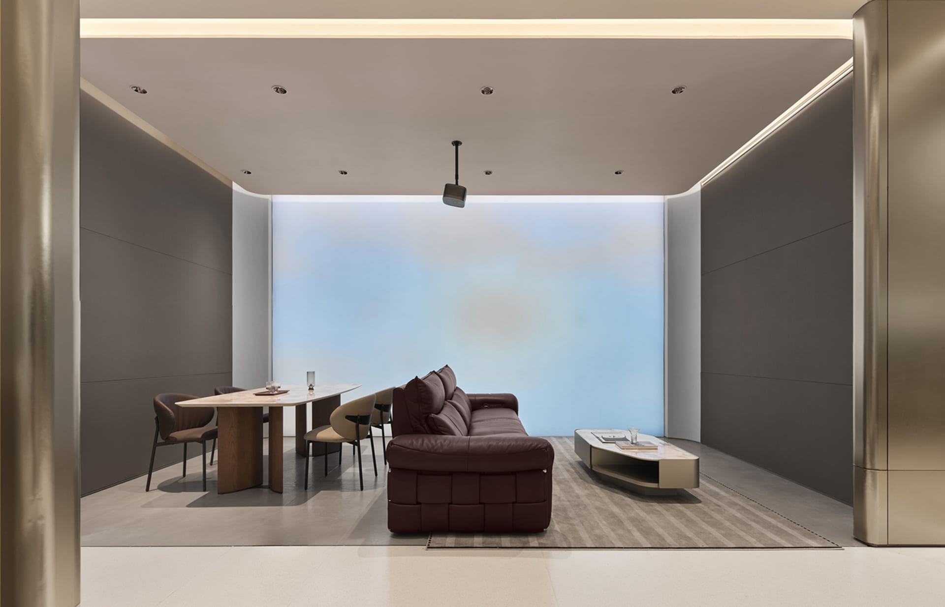 Modern minimalist living and dining room featuring a brown leather modular sofa, light wood and marble dining table with beige chairs, and a large blue gradient accent wall.