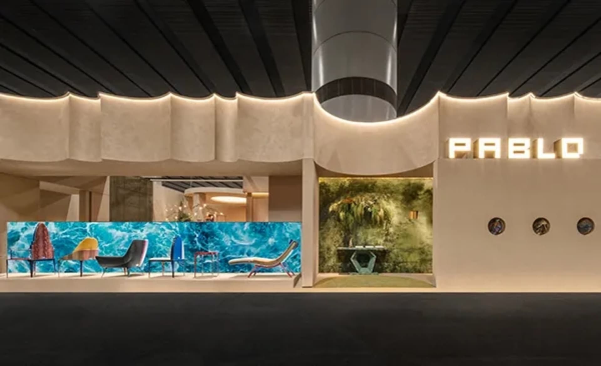 Pablo 現代展示間內部,特色為波浪形紋理灰泥牆搭配隱藏式照明,前方陳列色彩繽紛的休閒椅,背景有藍色波浪壁畫與苔蘚牆裝置。