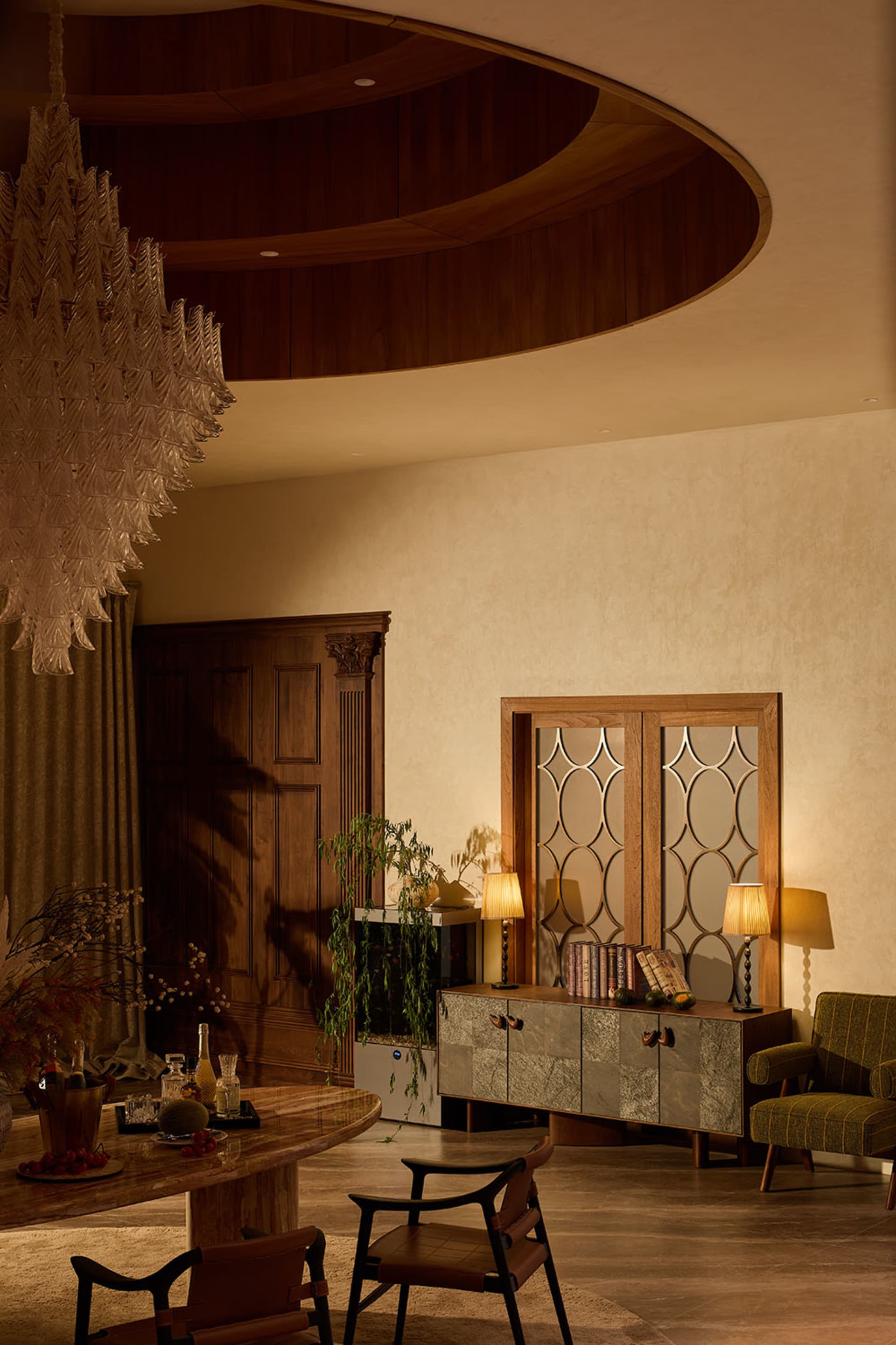 Luxurious dining room featuring a large curved walnut wood ceiling, dramatic white leaf chandelier, stone sideboard, and leather dining chairs under warm ambient lighting.