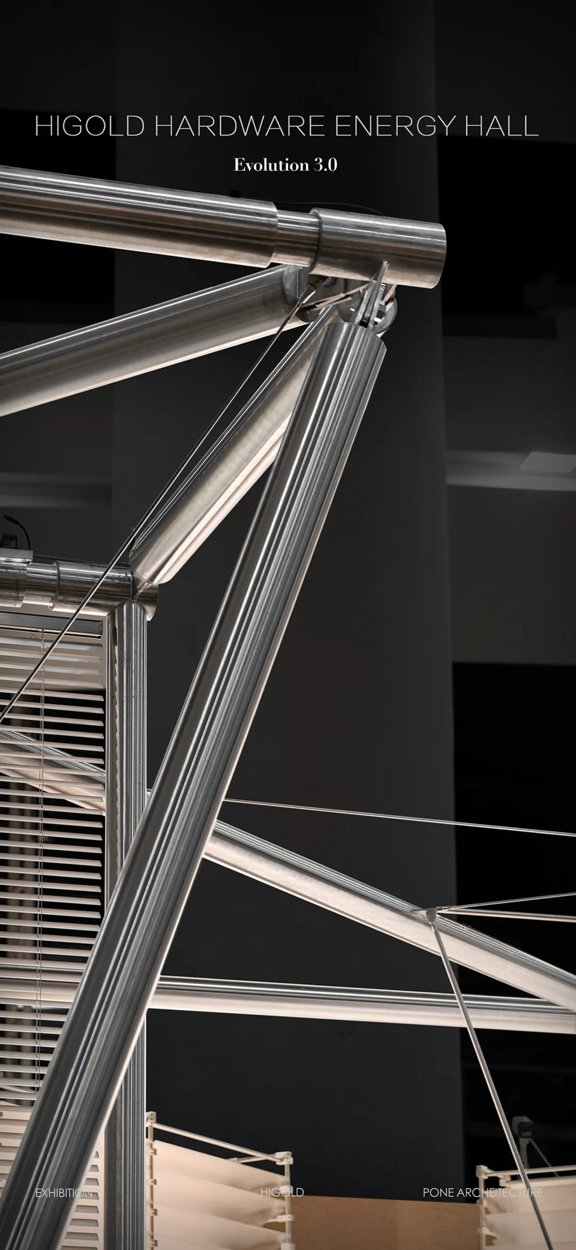 Close-up view of polished stainless steel pipes and mechanical joints forming an architectural structure with tension cables and blinds in the background.