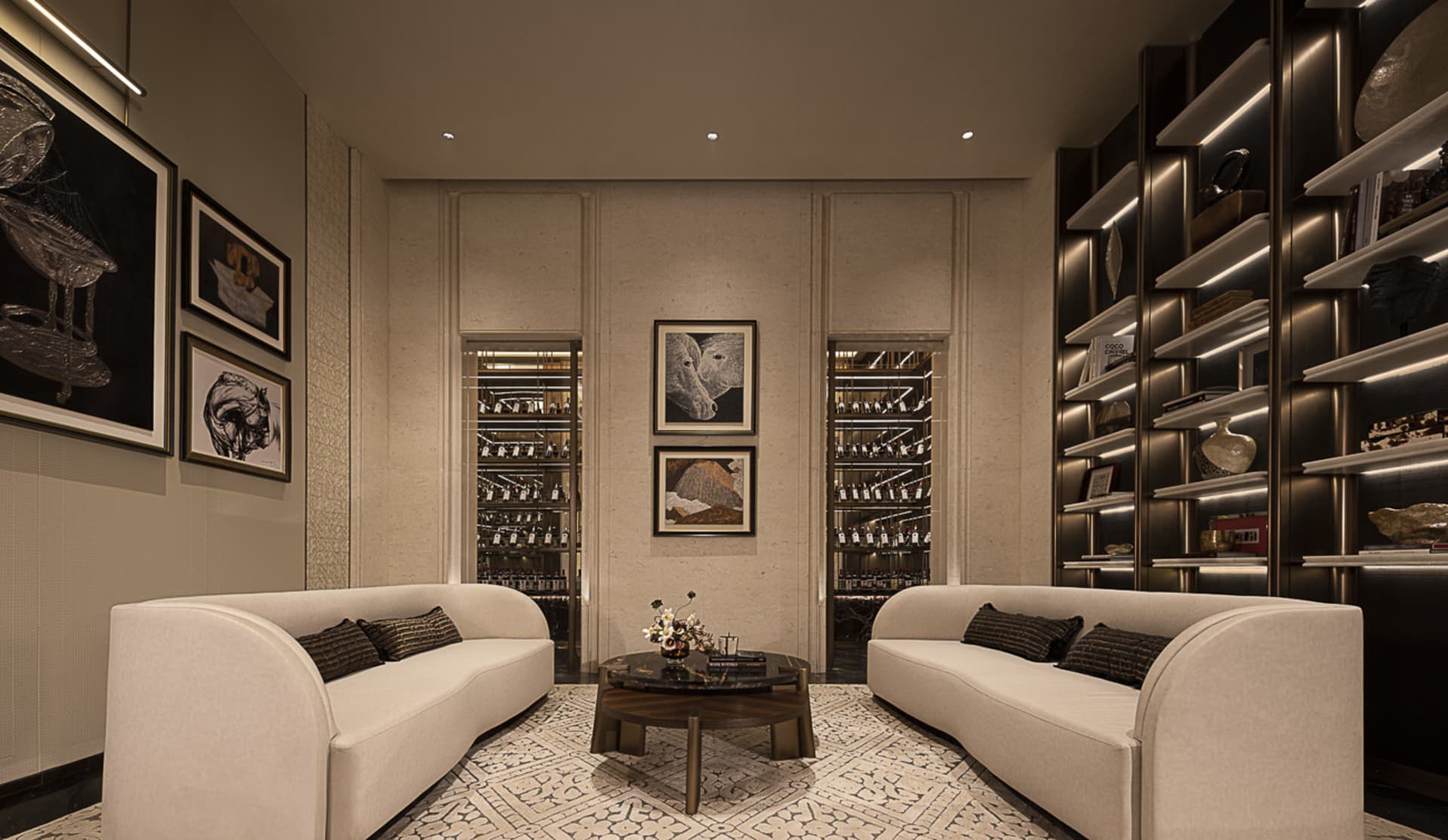 Modern luxury living room with two curved cream sofas, dark marble coffee table, patterned rug, and illuminated wine cellar display cases built into the back wall.