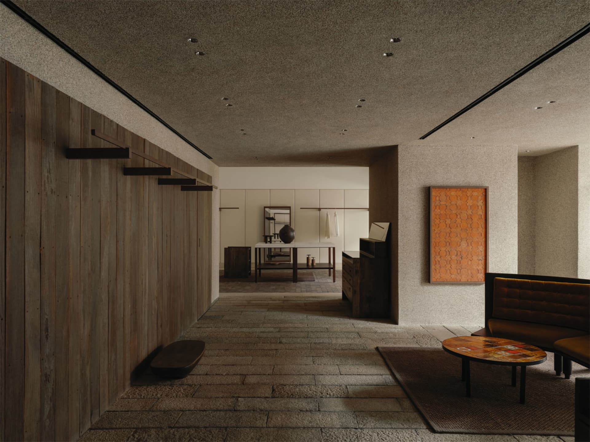 Modern minimalist entryway hallway with vertical wood paneling on the left, textured plaster walls, stone tile floor, built-in wooden bench, and a mustard-yellow upholstered banquette on the right.