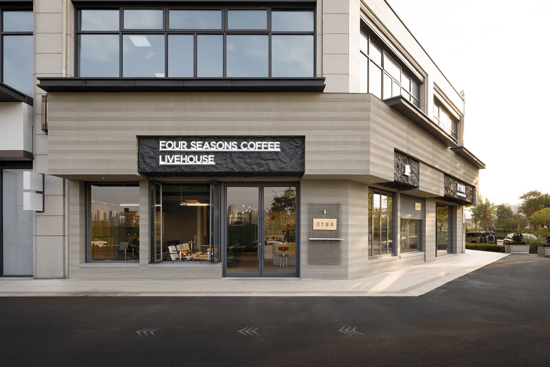 Modern corner commercial building with horizontal travertine stone cladding, large glass windows, and black textured signage for Four Seasons Coffee Livehouse.