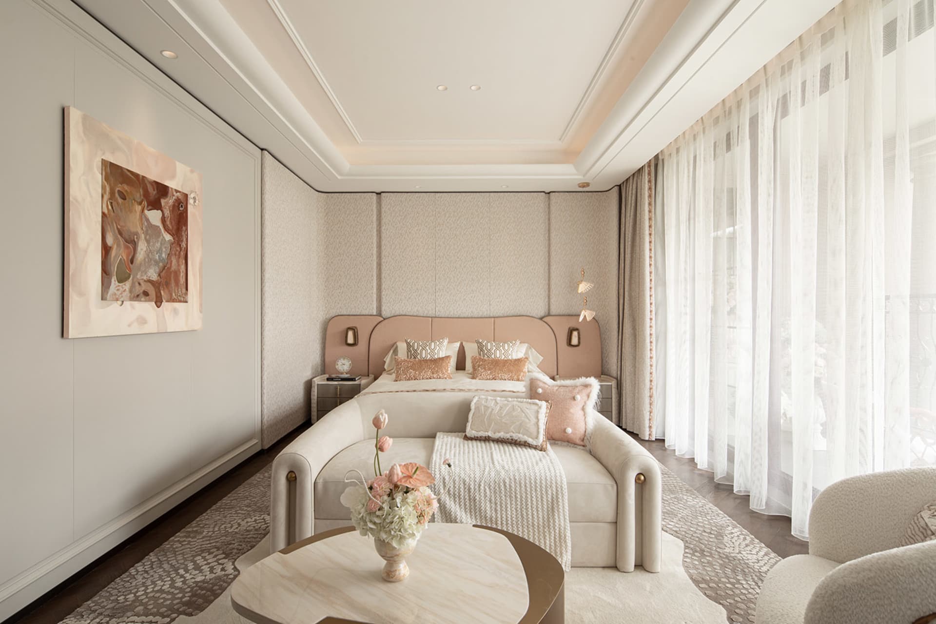 Modern luxury bedroom with blush pink upholstered bed, cream boucle sofa, marble coffee table, abstract wall art, and sheer white curtains allowing soft daylight.
