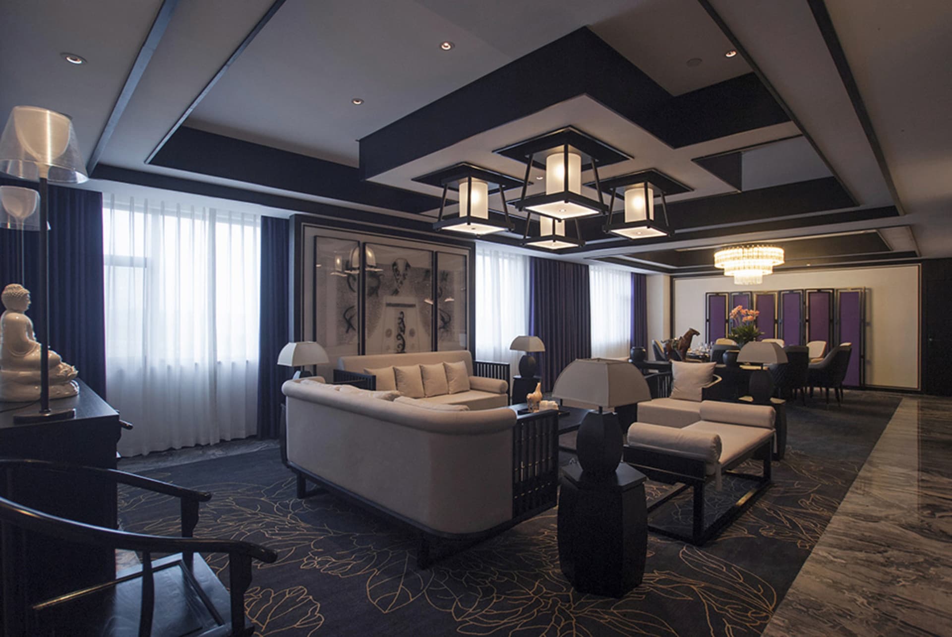 Modern luxury living room featuring dark wood ceiling beams, white sofas, marble floor, large Buddha statue, and crystal chandelier.