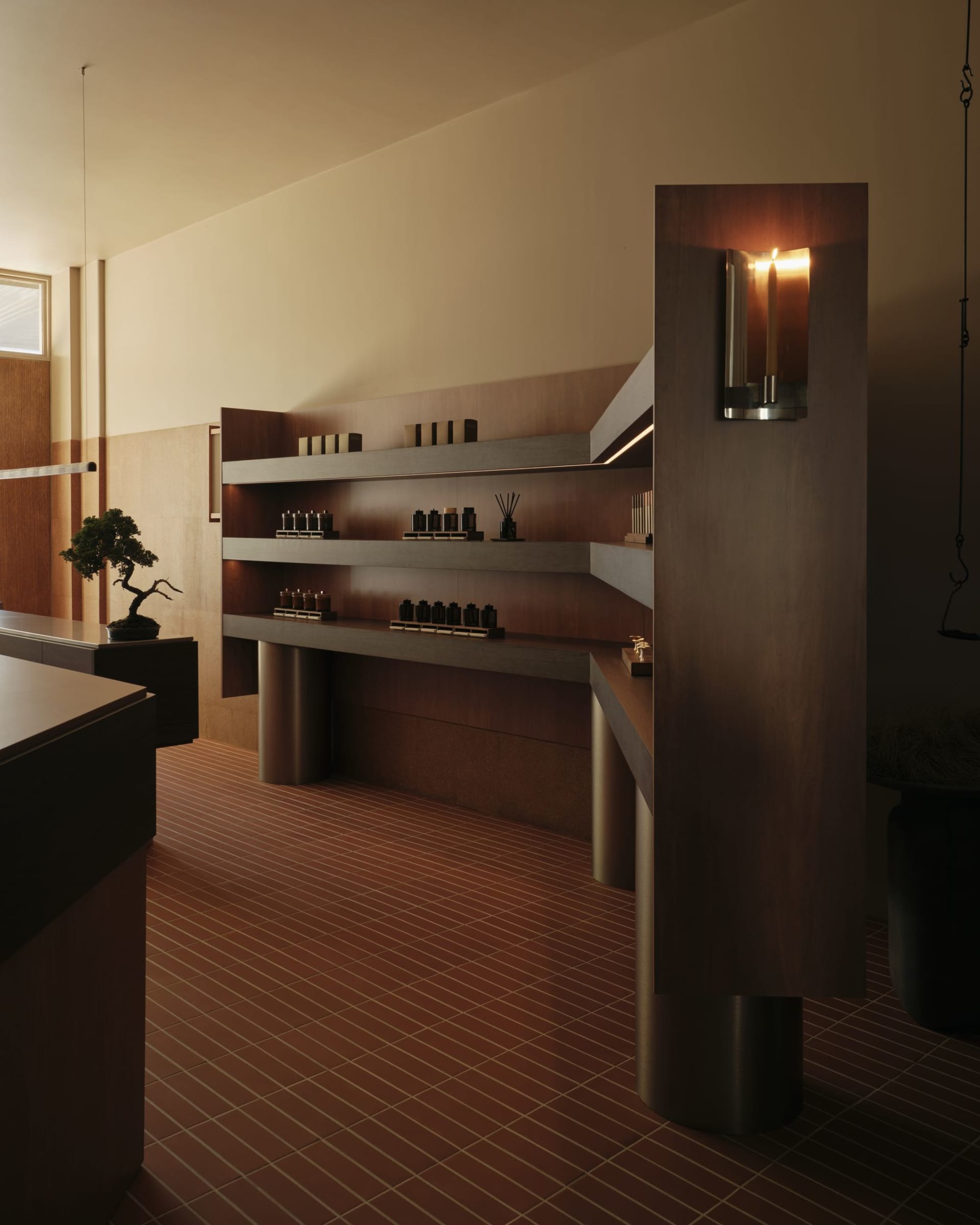 Modern minimalist interior featuring a floating walnut wood console with integrated shelves, terracotta floor tiles, and warm wall sconce lighting.