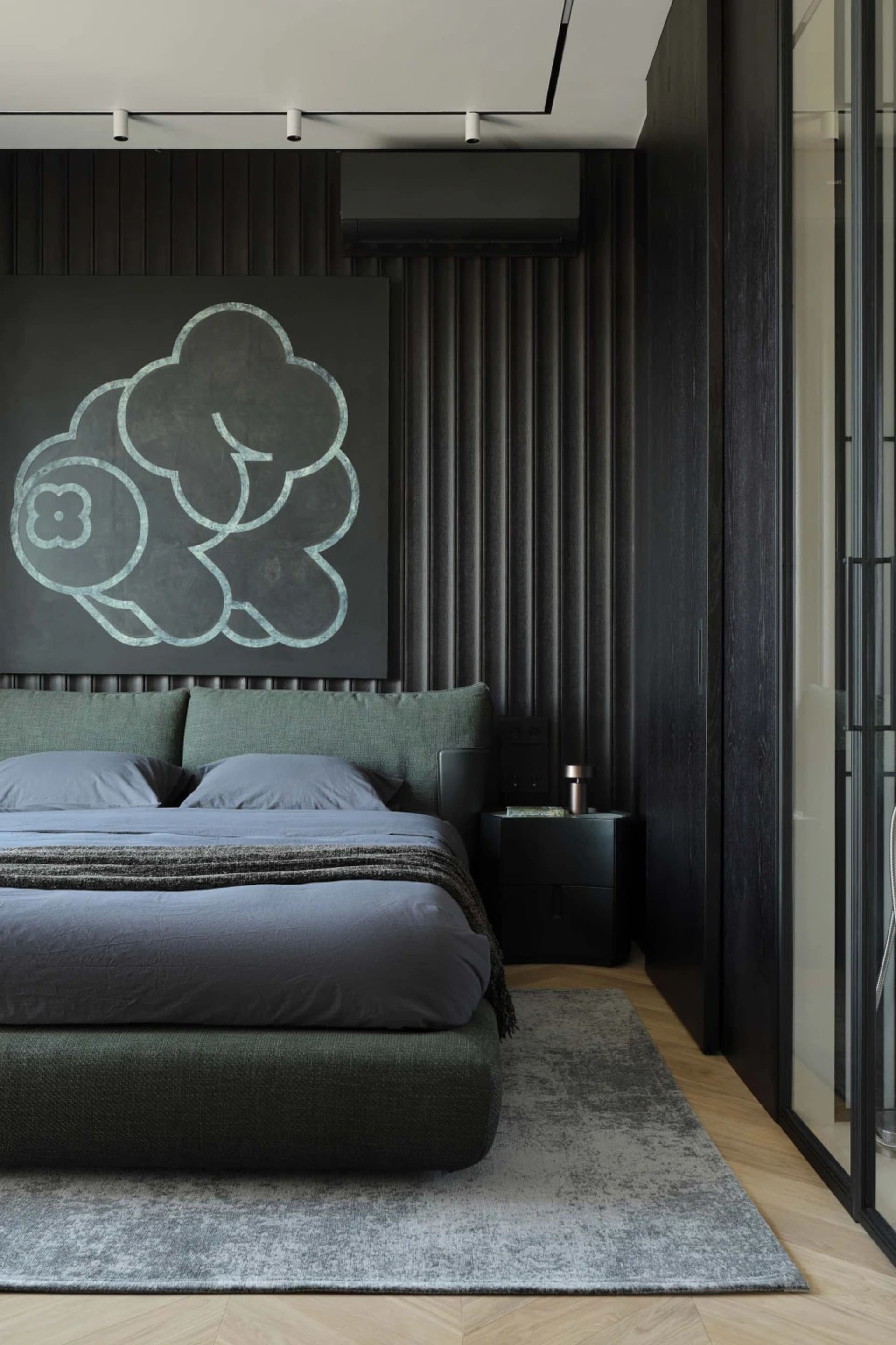 Modern dark-toned bedroom with sage green upholstered bed, large cloud-shaped artwork in teal on black wall, wood herringbone floor and grey area rug.