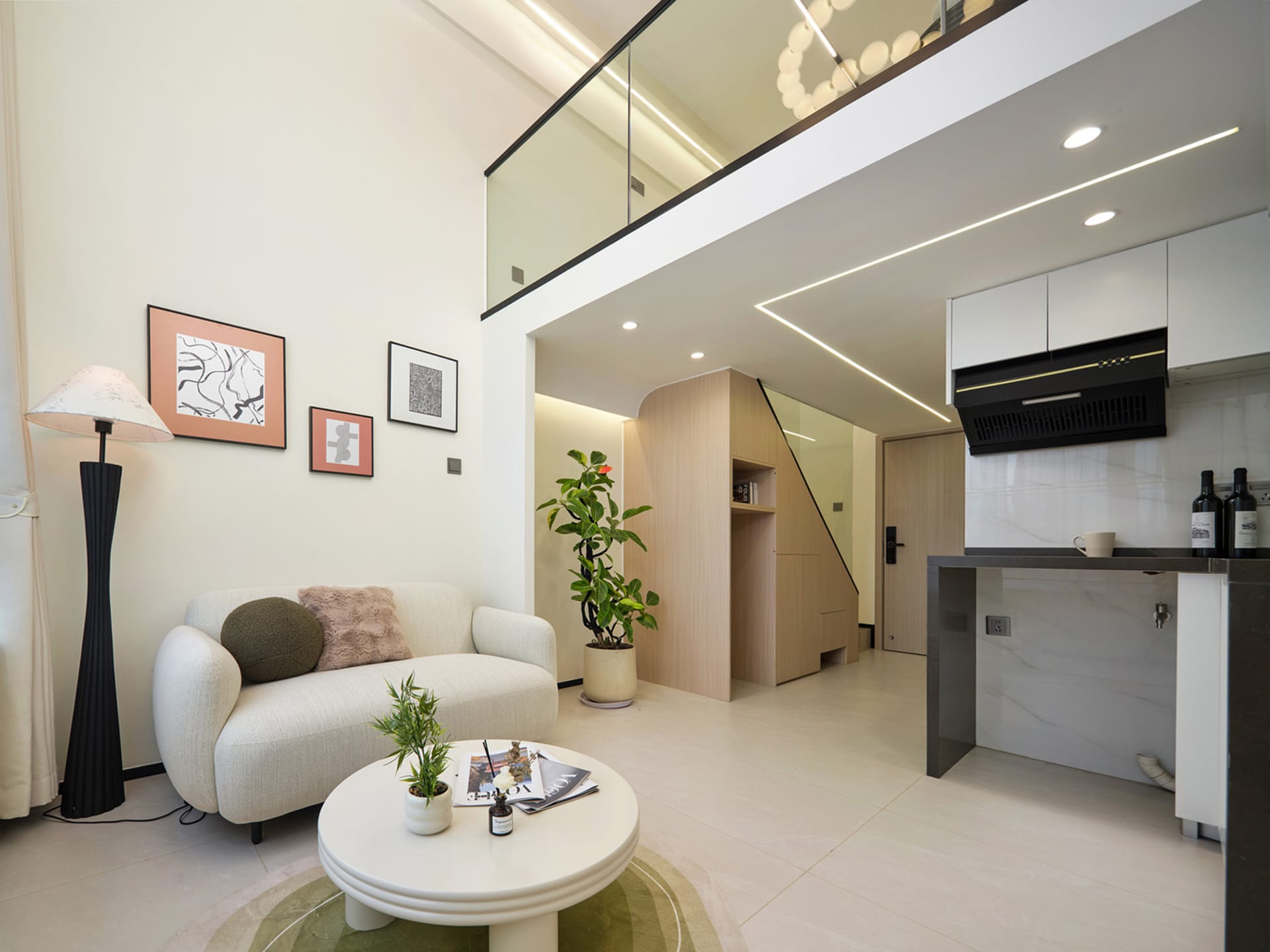 Modern double-height living room with white sofa, round coffee table, light wood cabinetry, marble kitchen island, and glass railing on the upper floor.