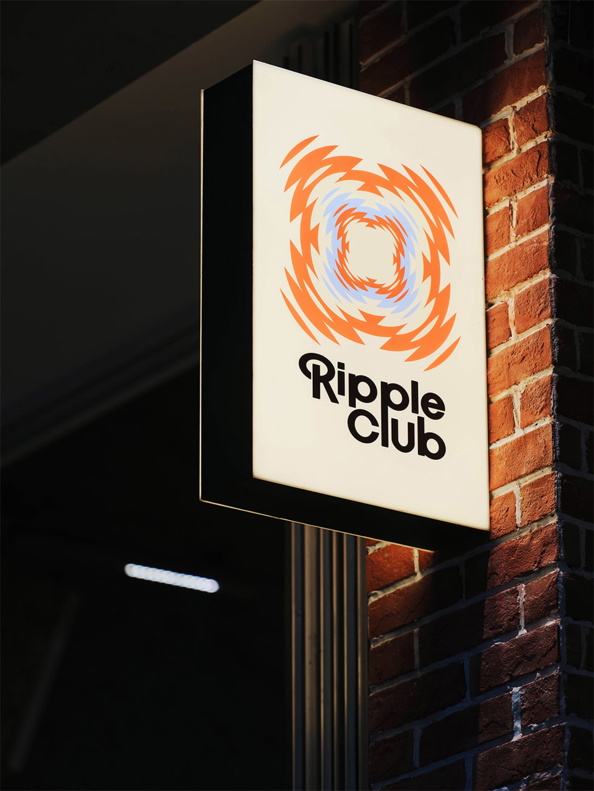 Illuminated rectangular sign with Ripple Club logo and text, mounted on a red brick wall at night.