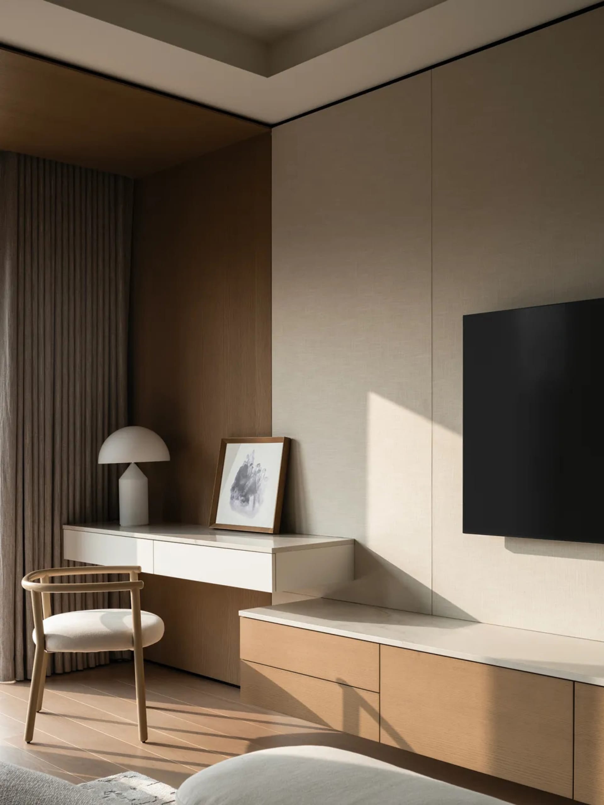 Modern minimalist living room corner featuring a light oak floating media console, white desk, upholstered chair, table lamp, and wall-mounted TV under warm natural light.