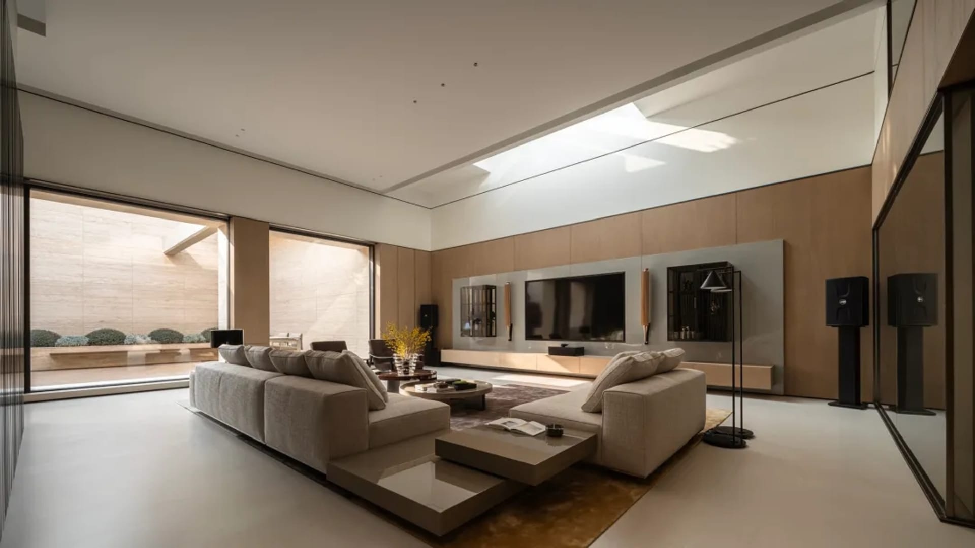 Modern minimalist living room featuring a large L-shaped beige sectional sofa, low wooden coffee table, oak wall paneling, large wall-mounted TV, and a long skylight allowing abundant natural light.