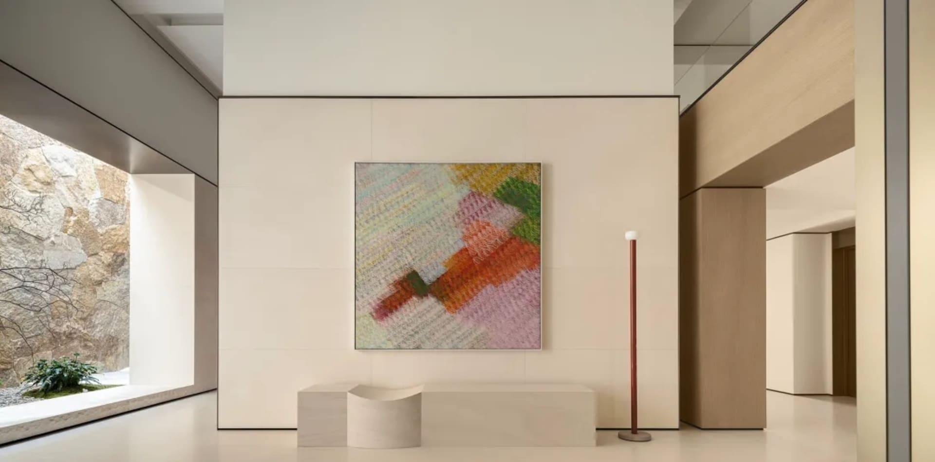 Modern minimalist entryway with large colorful abstract painting, curved concrete bench, wooden floor lamp, and natural stone garden view.