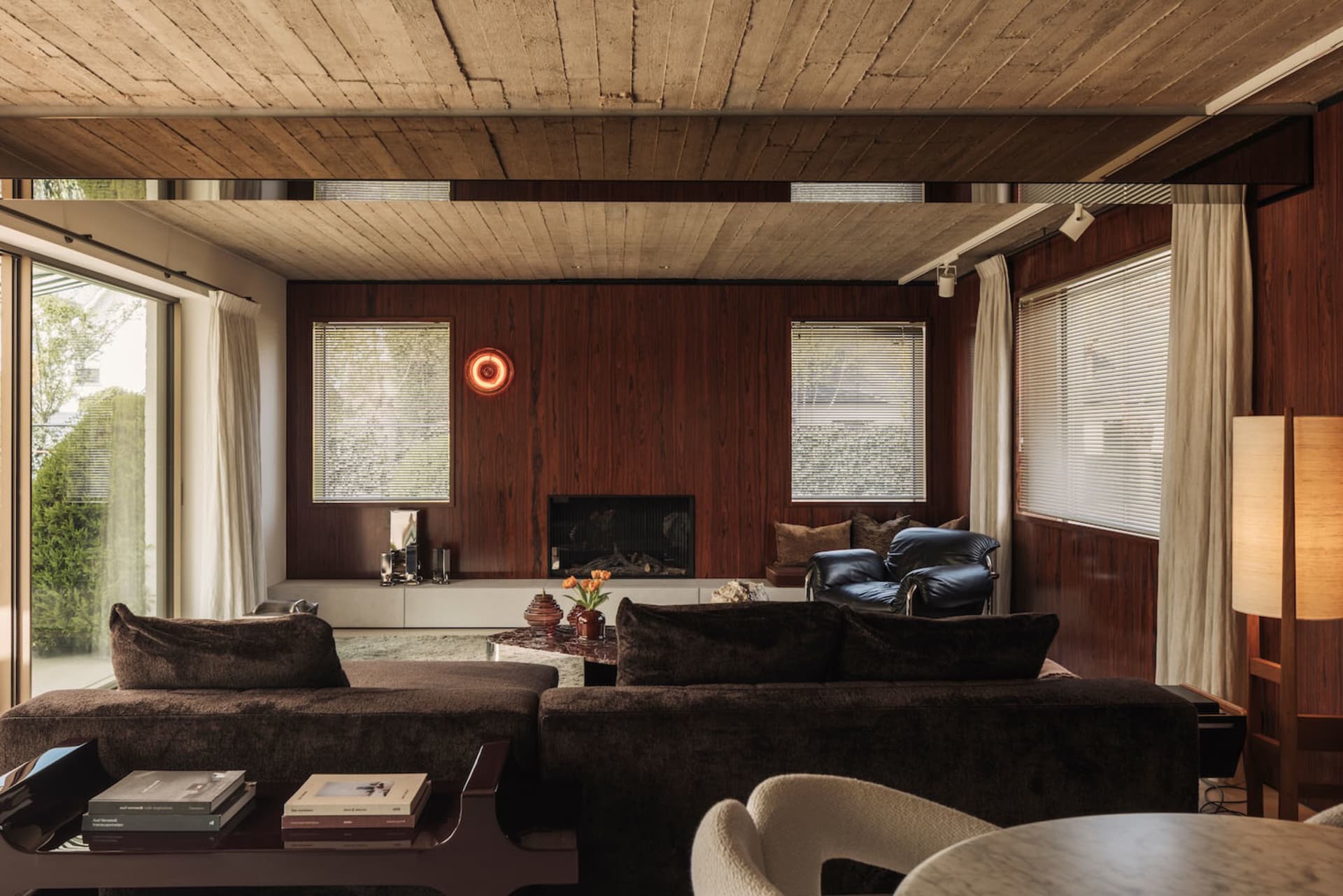 Mid-century modern living room with dark walnut wood paneling, brown velvet sectional sofa, leather lounge chairs, and a wooden ceiling.