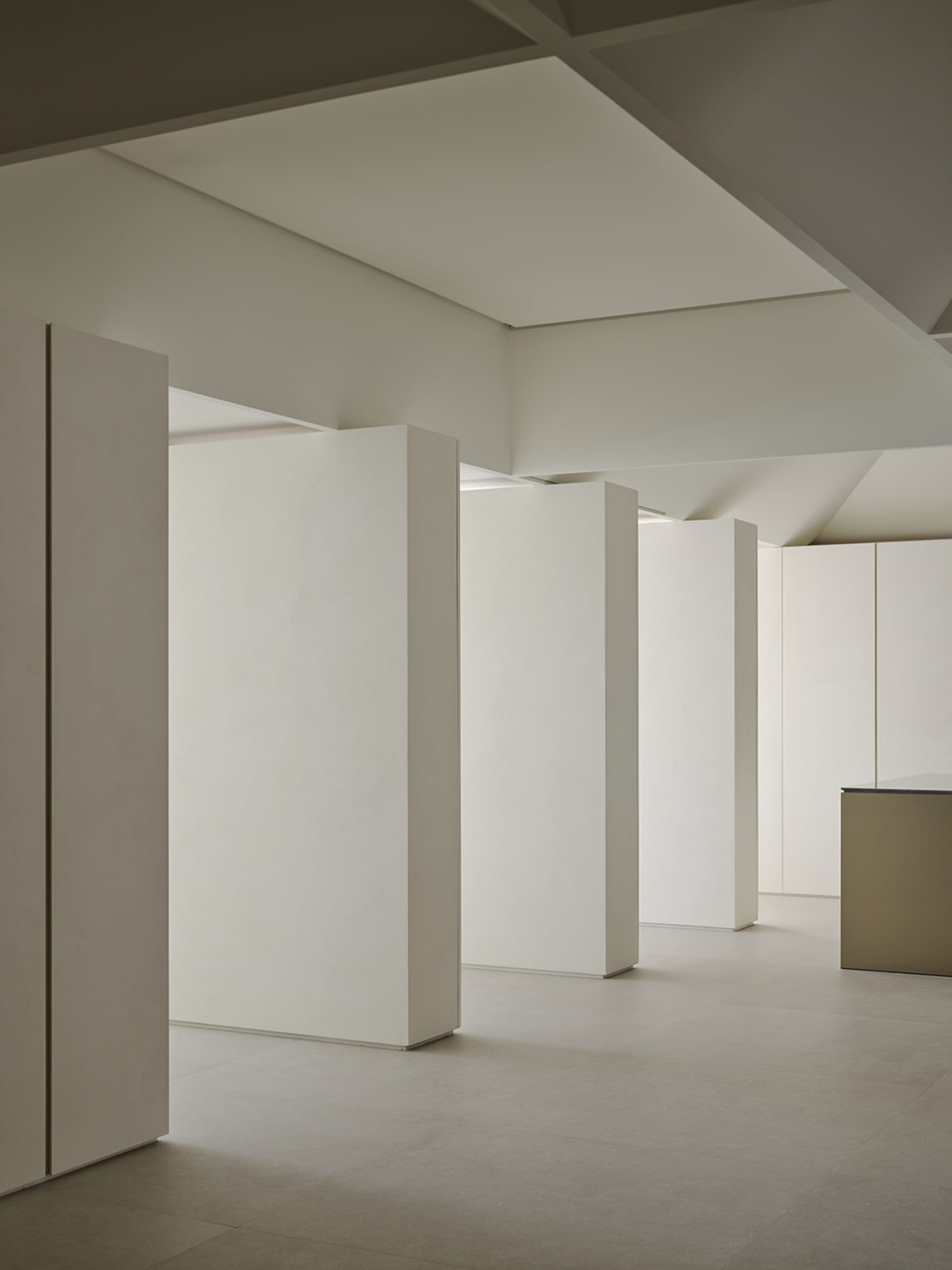 Minimalist interior space featuring multiple white vertical volumes, micro-cement floors, and dramatic geometric ceiling with hidden lighting.