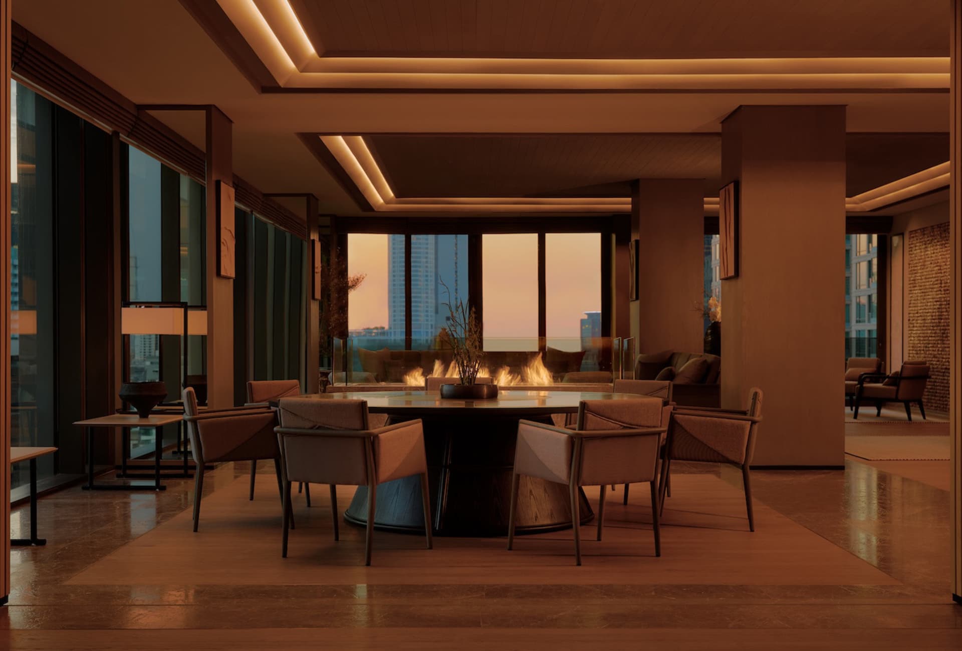 Modern luxury dining room featuring a large round walnut dining table with six upholstered chairs, warm cove lighting, and floor-to-ceiling windows showing a city skyline at sunset with a fireplace in the background.