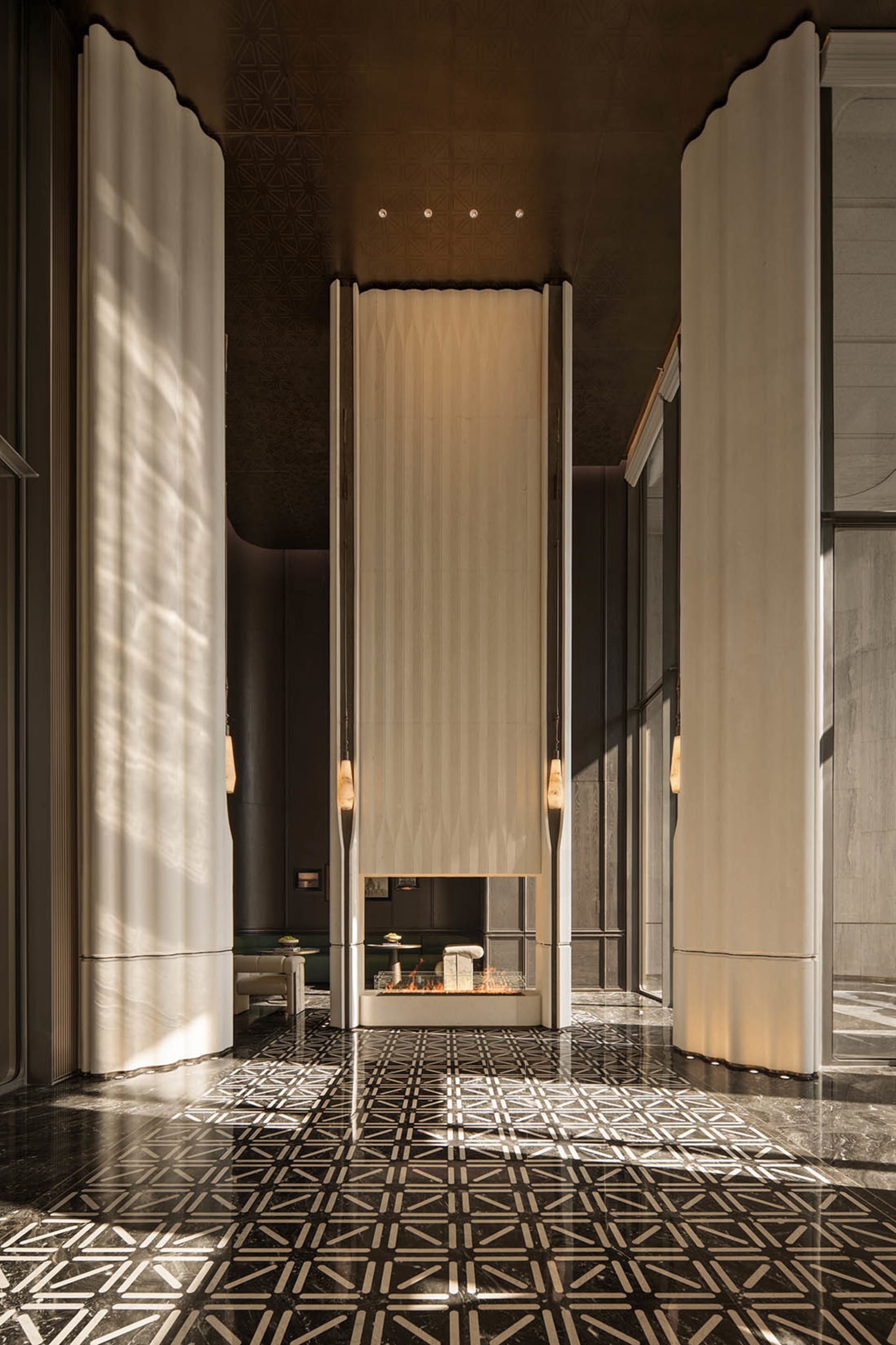 Luxurious hotel lobby featuring a tall central fireplace with lit fire, dramatic floor-to-ceiling curtains, and a polished black marble floor with white geometric pattern.