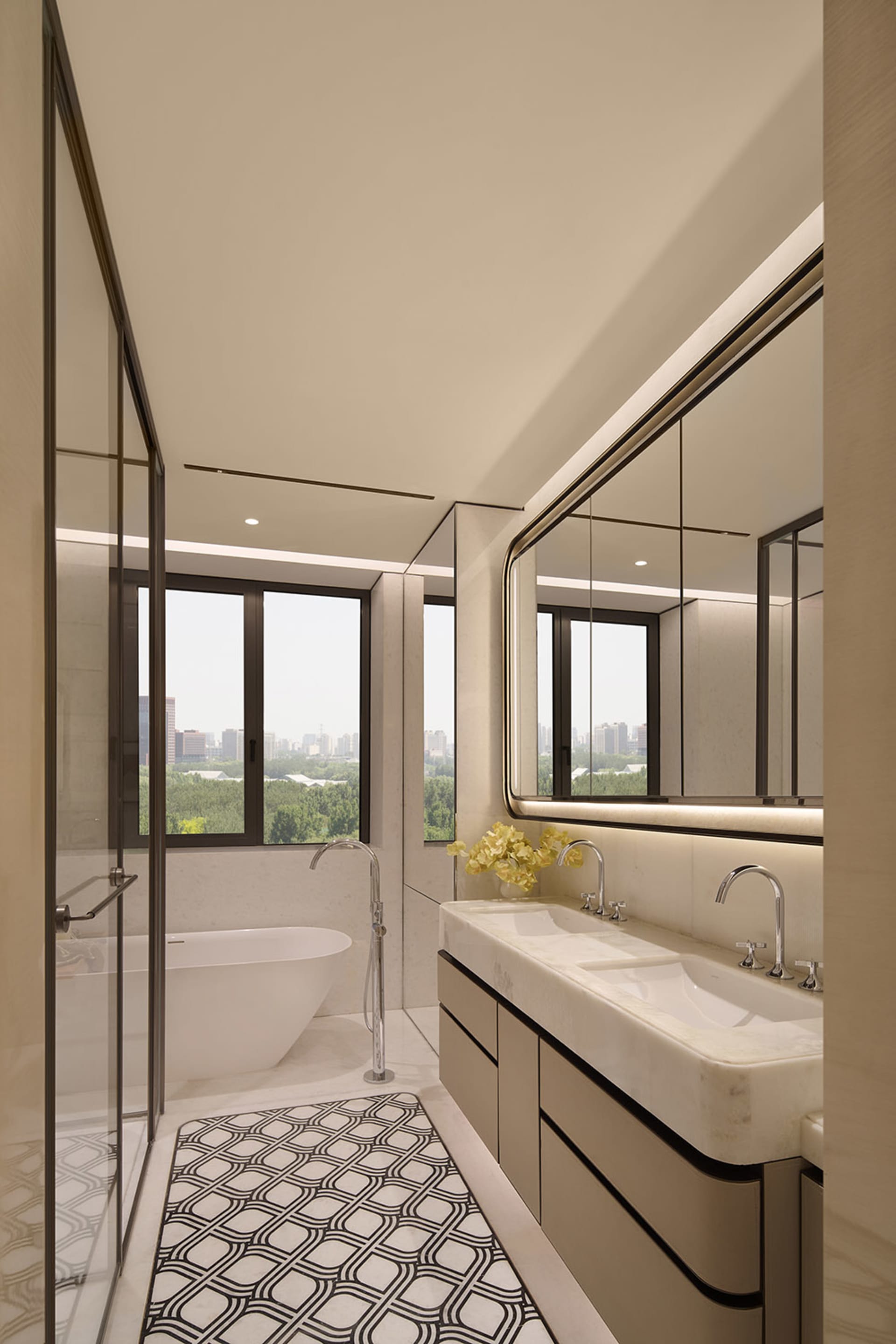 Modern luxury bathroom interior with white marble double vanity, freestanding bathtub, black-framed glass shower, and large windows overlooking a green cityscape.