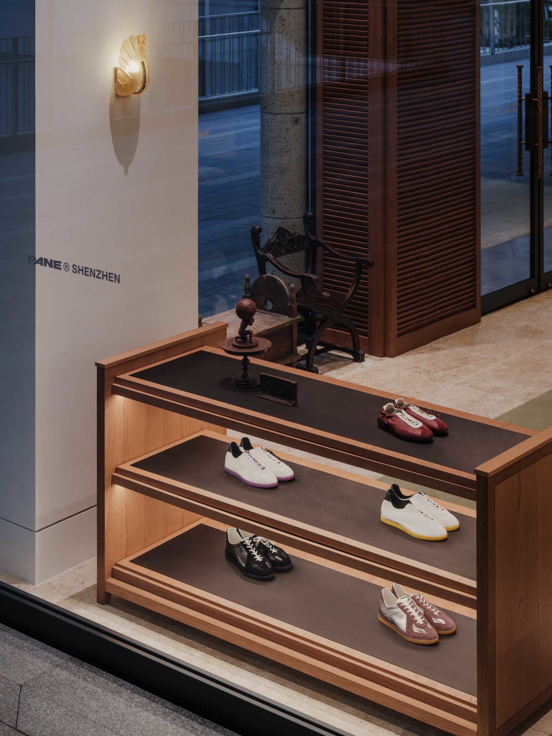 Multi-tiered oak display shelf with integrated lighting showcasing various luxury sneakers inside a modern Shenzhen retail store.