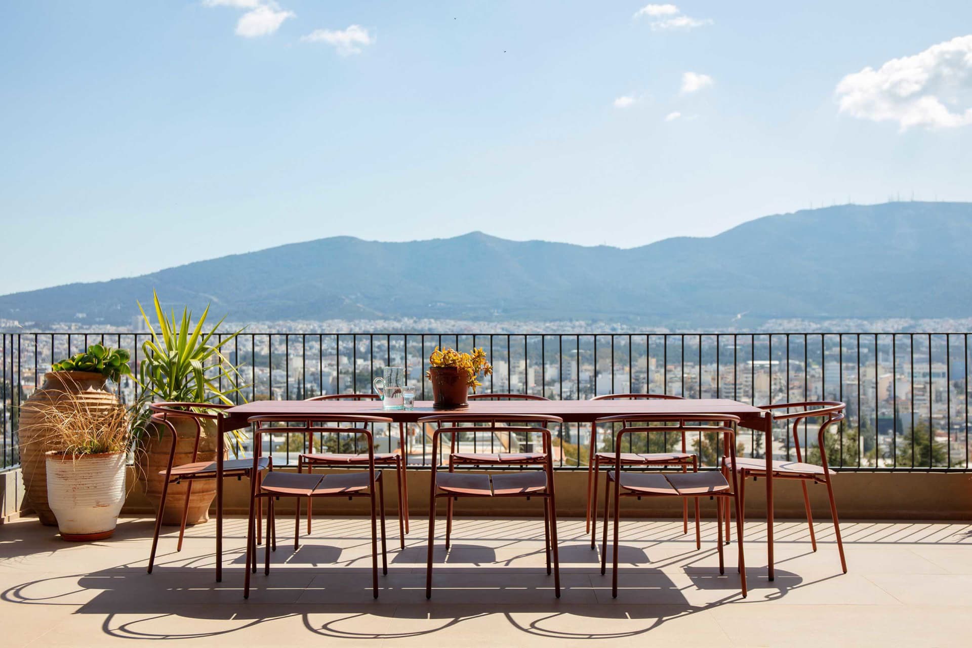 Outdoor dining table and six chairs in terracotta color on a rooftop terrace overlooking a vast mountain range and cityscape