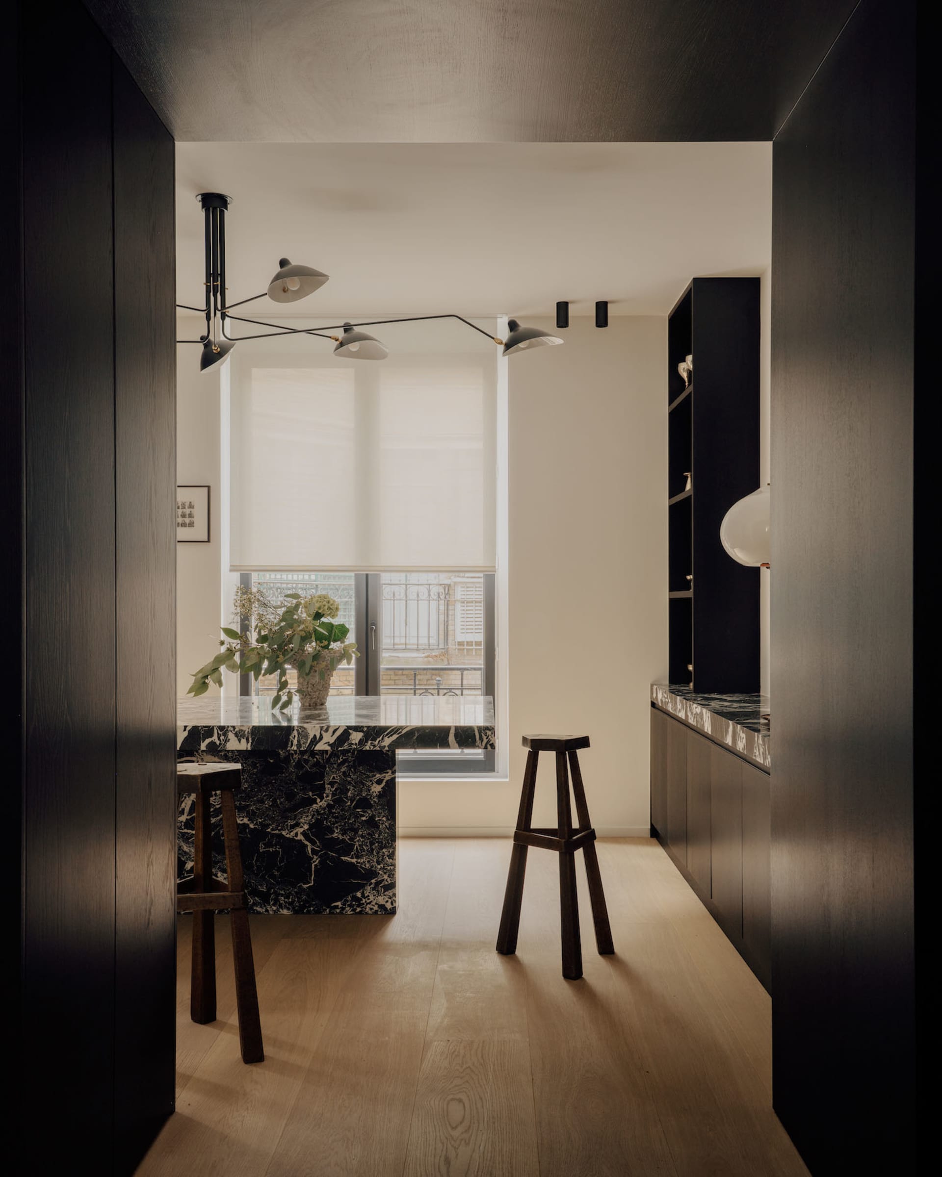 Modern minimalist kitchen featuring a black and white marble island, dark wood cabinetry, wooden stools, and a large window with natural light.