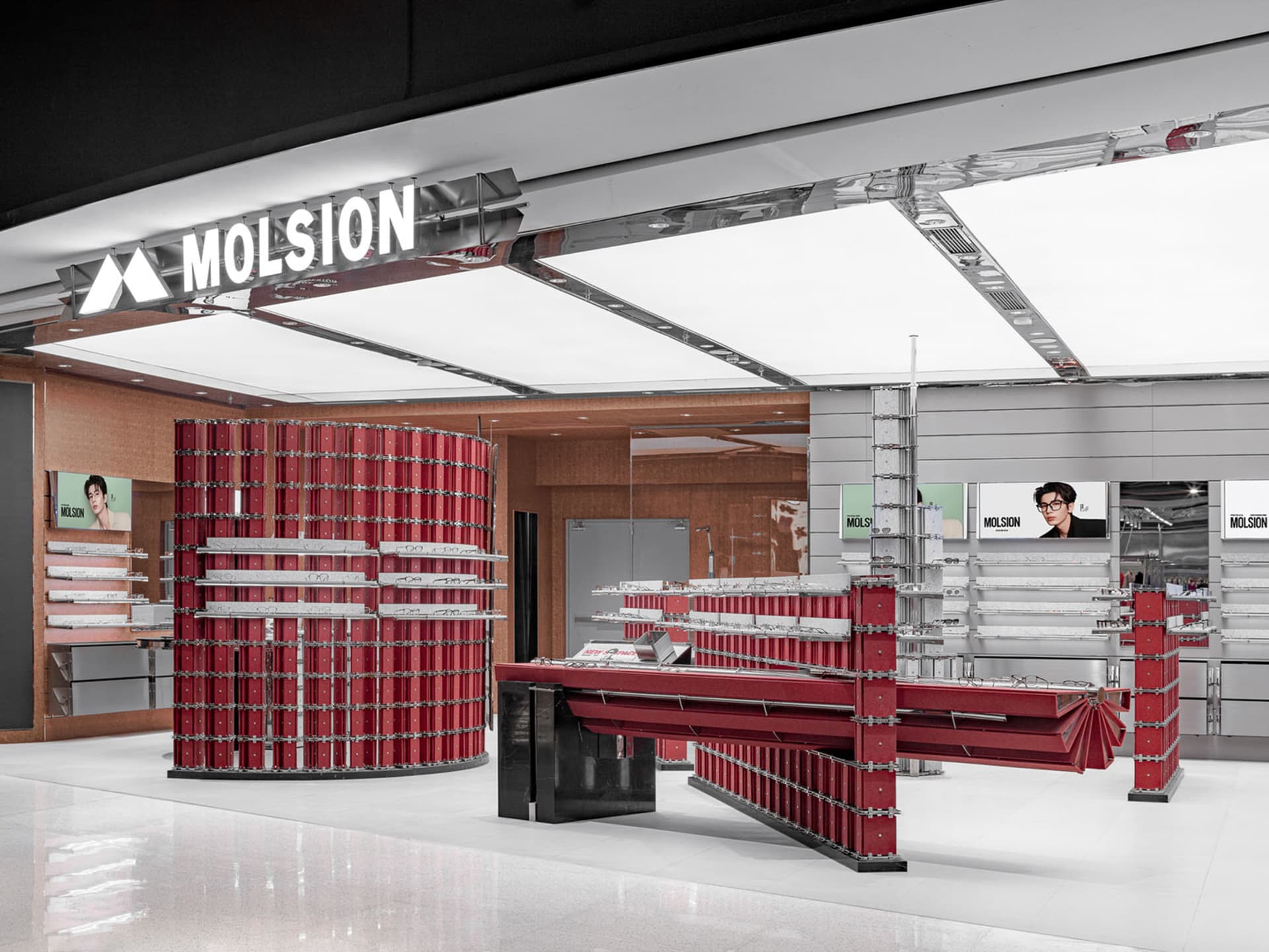 Modern optical store interior featuring striking red modular display towers and tables with metal frames, white glossy floor, and bright ceiling lighting.