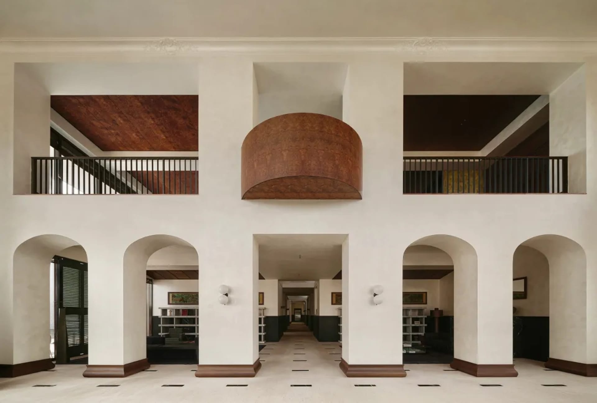 A grand double-height entrance hall featuring white walls, dark wood baseboards, multiple arches, and a large curved burl wood canopy suspended in the center.