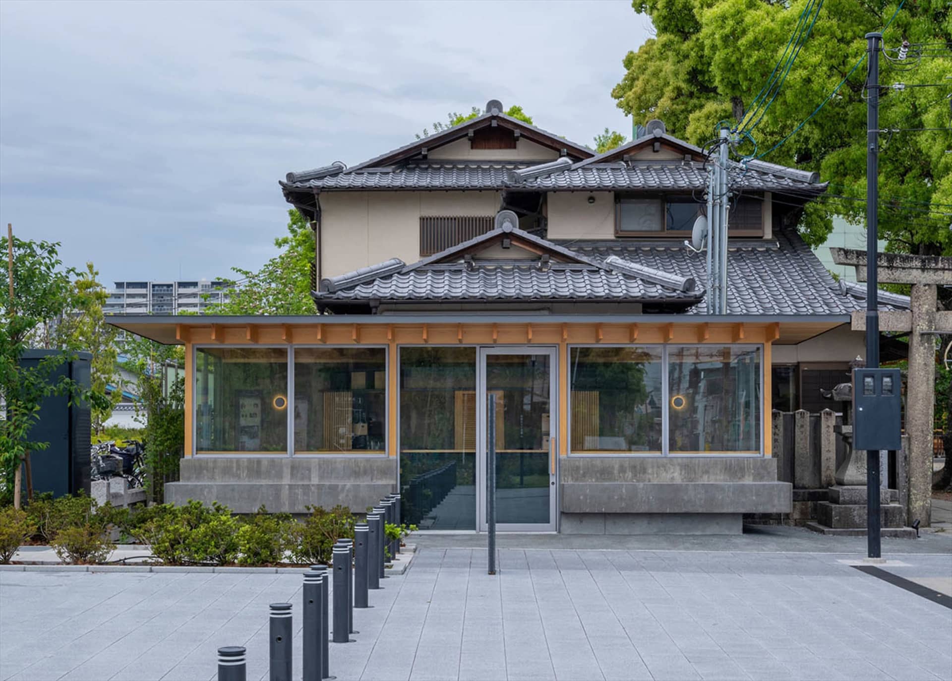 這棟兩層樓日式住宅正面,地面層為現代玻璃立面,搭配傳統瓦片屋頂與混凝土基座,坐落於鋪面整齊的都市街道上。