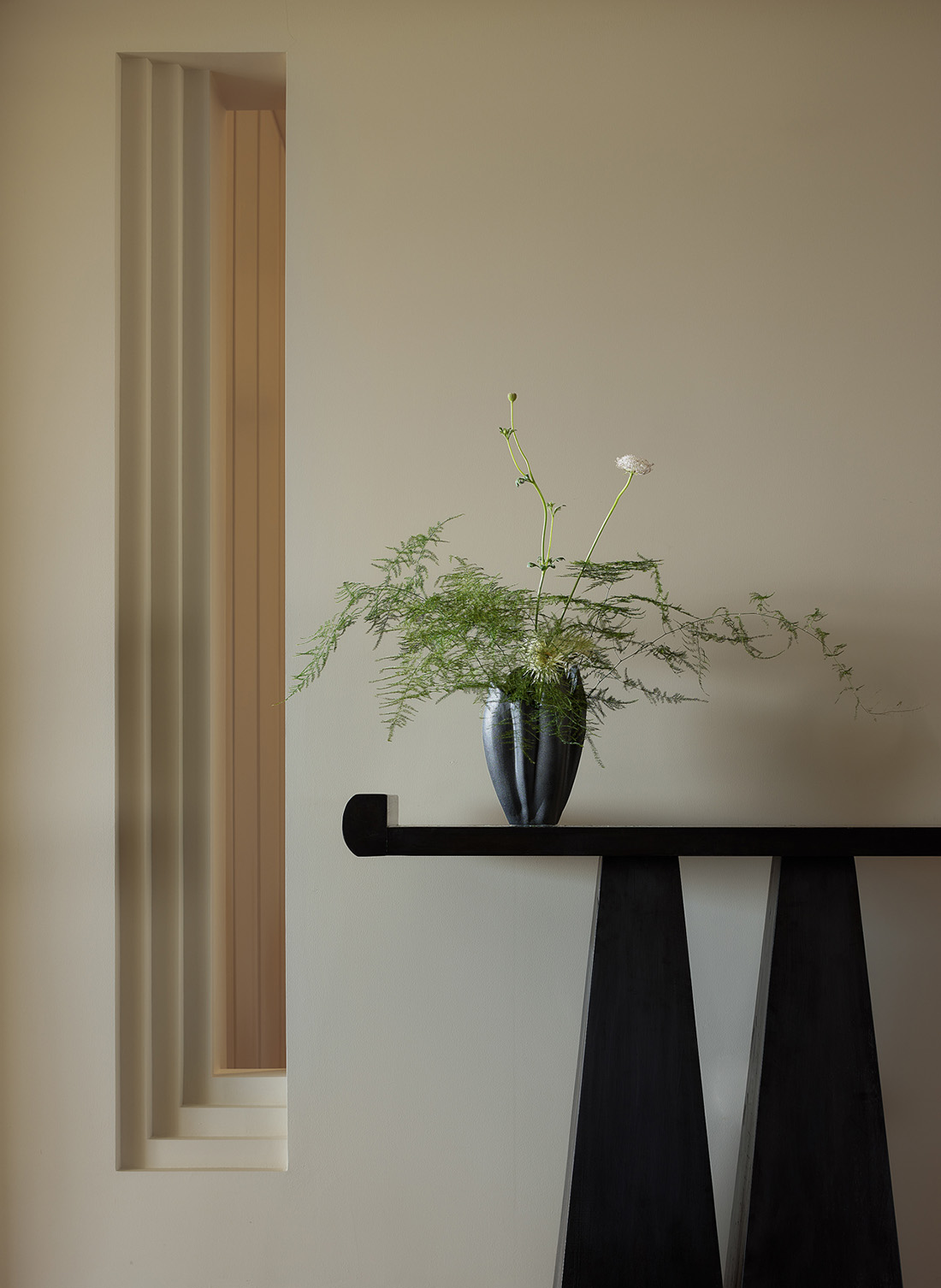 Minimalist interior with a single curated plant arrangement, matte black accents, and warm neutral tones.