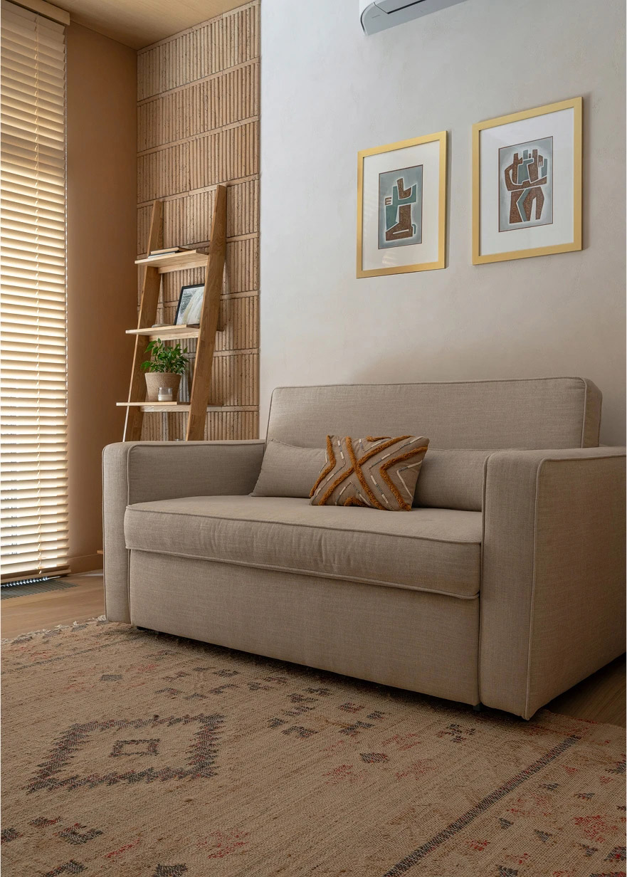Beige linen sofa with a rust patterned cushion, a wood ladder shelf, and a warm patterned rug.