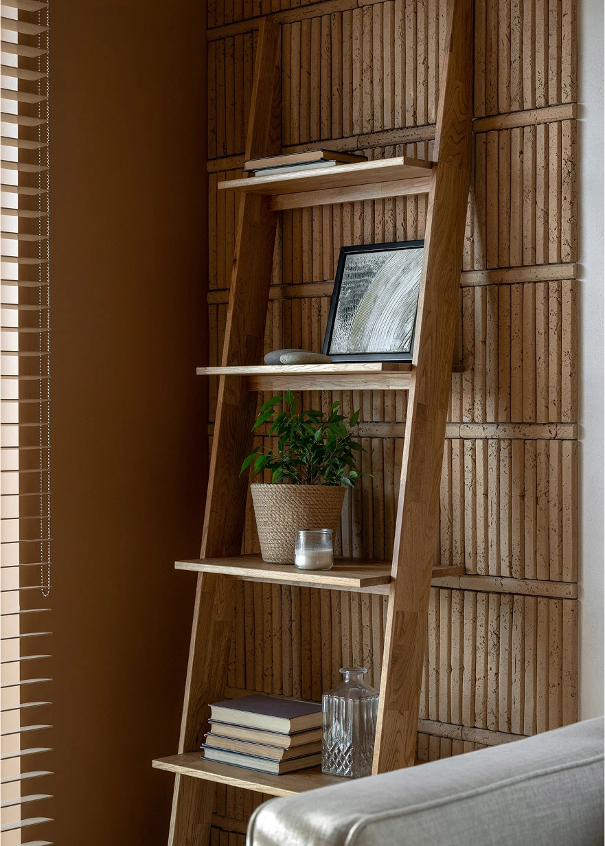 Wood ladder shelf against a terracotta wall holding books, a plant, and a candle.