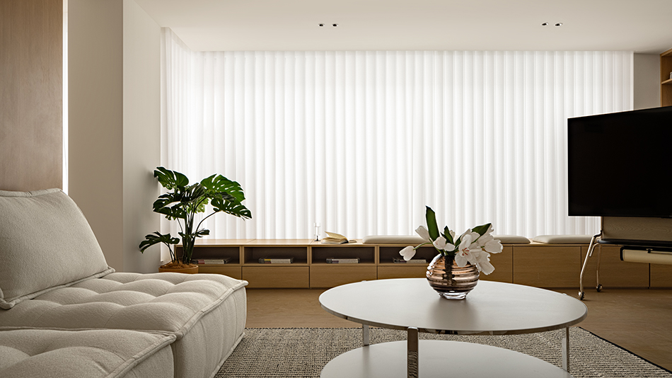 Modern cozy living room with plants, large windows, and warm daylight in an apartment setting.