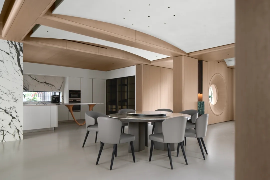 Modern kitchen with marble island, warm wood cabinetry, and open dining area in a minimalist style.