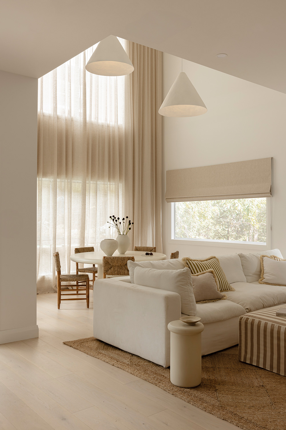 Contemporary neutral living room with white furniture and strong daylight entering through a large window.