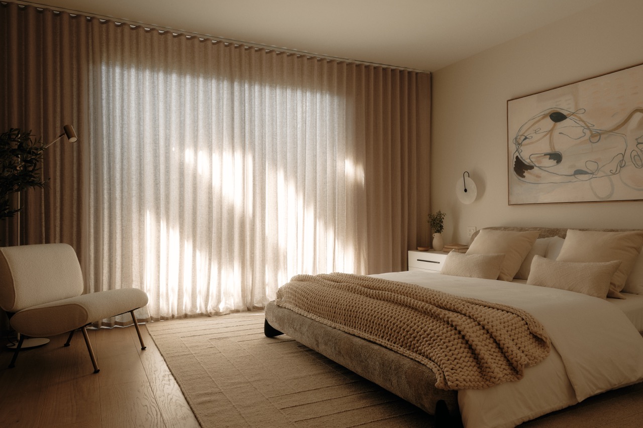 Neutral minimalist bedroom with low platform bed, sheer curtains filtering soft natural light, and uncluttered floor space.