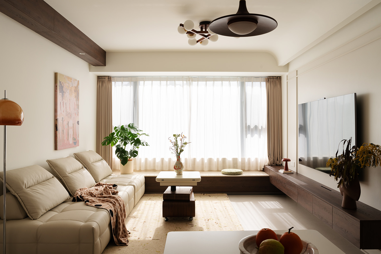 Warm neutral living room with a beige sofa, terracotta lamp, dark wood beam, and dried floral accents.