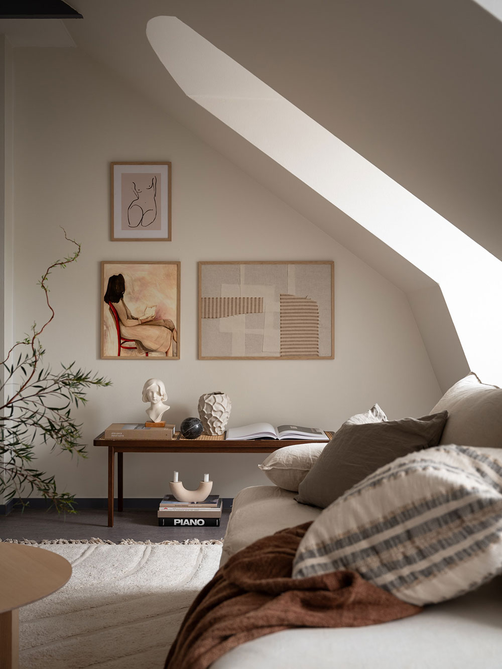 Modern minimalist living room in warm neutral tones with soft seating by a window, evoking a cozy reading nook.