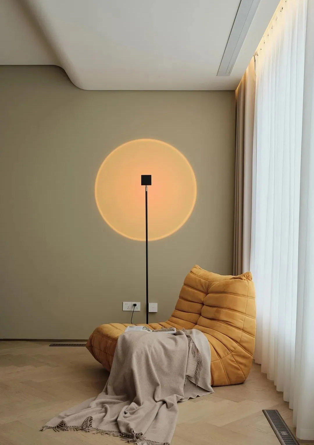 Mustard velvet lounge chair beside a glowing warm-toned floor lamp, throw blanket, and open book.