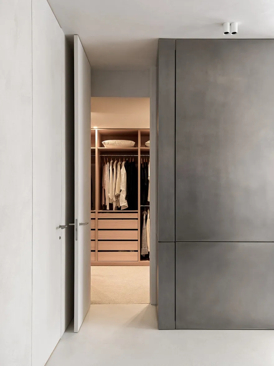 Small minimalist walk-in closet with warm neutral wood wardrobe and clean built-in storage.