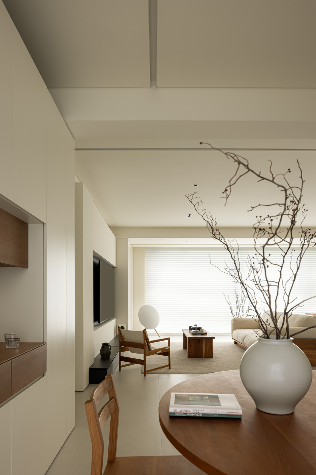 Minimalist living room with warm wood shelving, glass accents, and a neutral beige sofa in a clean modern apartment.