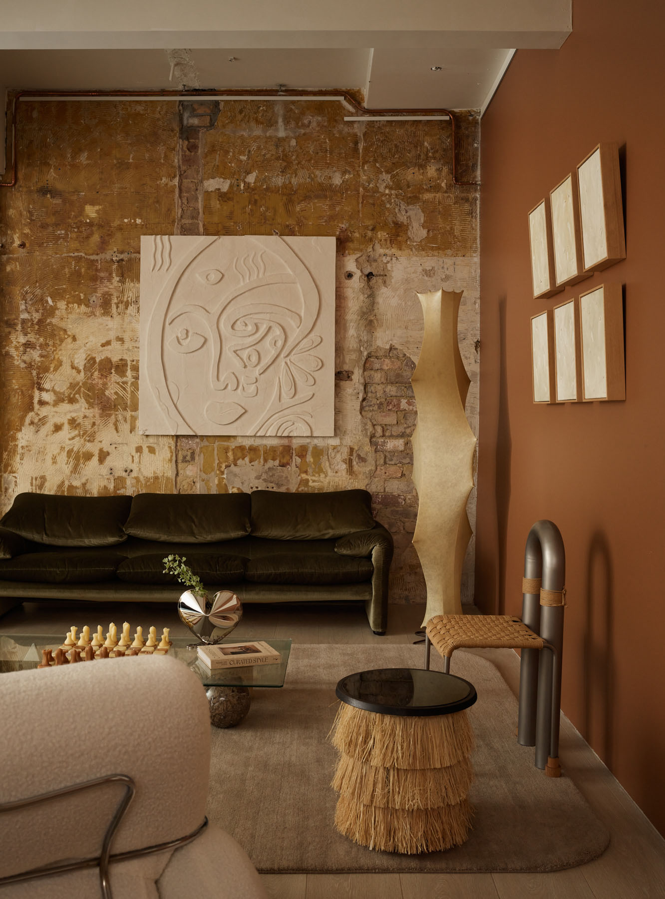 Living room with a moss green sofa against a warm copper accent wall, rattan chair, and terracotta tones.