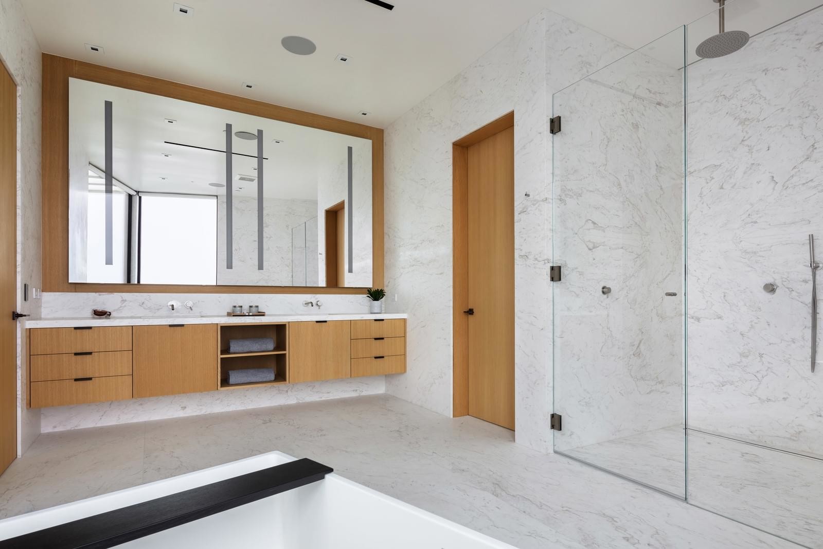 Bright modern bathroom with warm marble walls, open shower area, and natural light flooding through large windows.